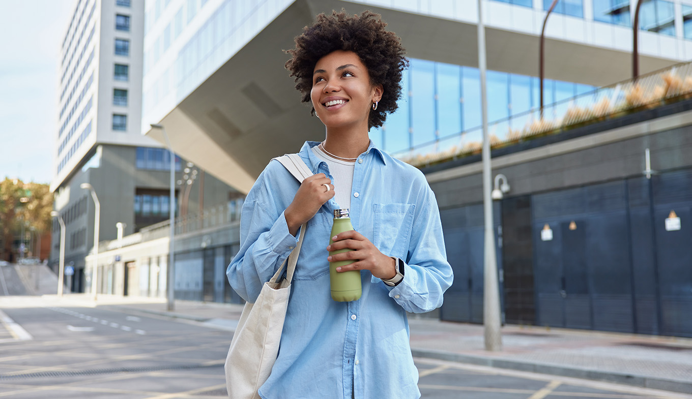 Happy curly haired woman carried fabric bag holds fresh water in bottle Happy curly haired woman carried fabric bag holds fresh water in bottle