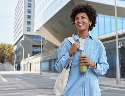 Happy curly haired woman carried fabric bag holds fresh water in bottle Happy curly haired woman carried fabric bag holds fresh water in bottle
