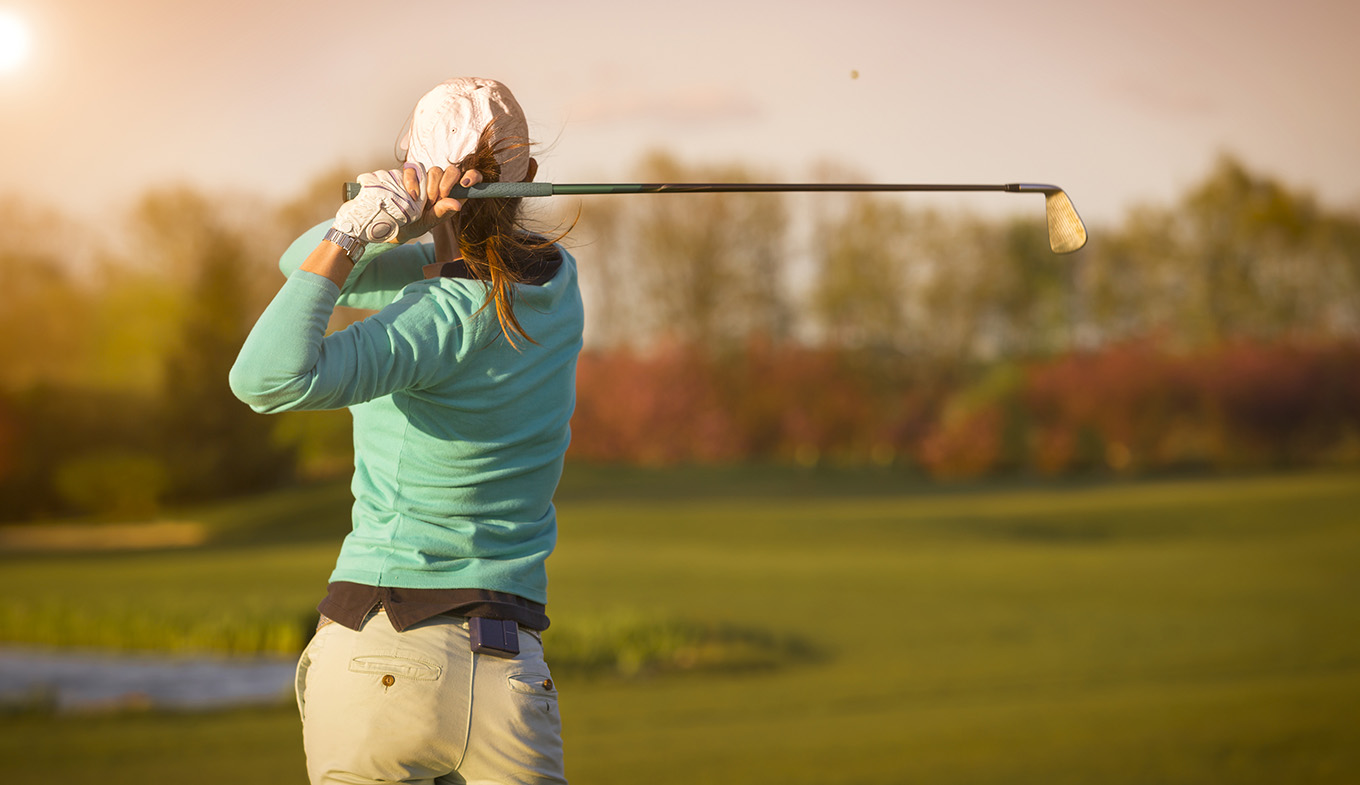 Female golfer swinging golf club on fairway during sunset Female golfer swinging golf club on fairway during sunset