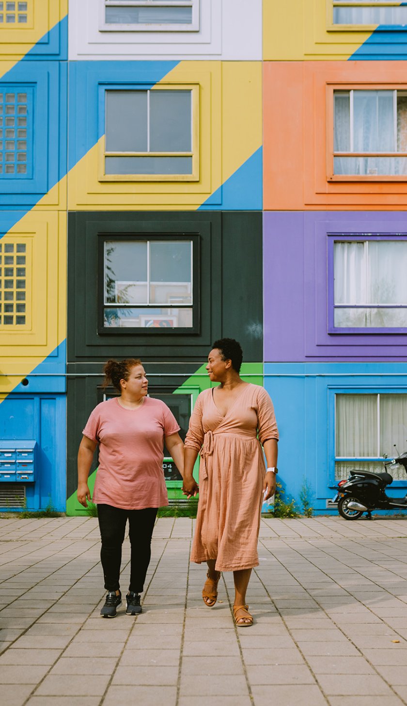 Couple walking hand in hand in front of colorful housing complex in Heesterveld, Amsterdam Couple walking hand in hand in front of colorful housing complex in Heesterveld, Amsterdam