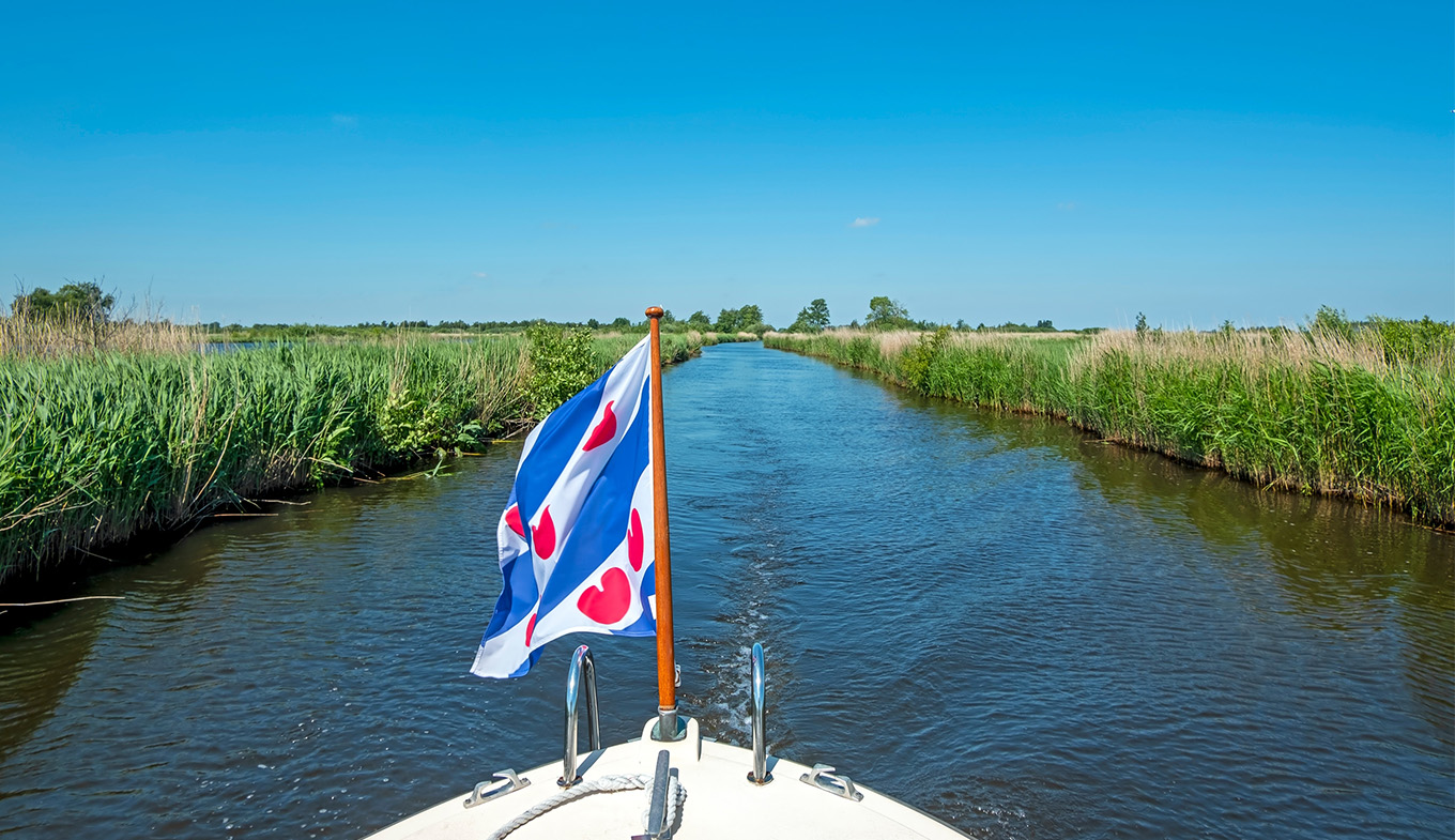 Boat with flag of Friesland sailing through the Alde Feanen National Park Boat with flag of Friesland sailing through the Alde Feanen National Park