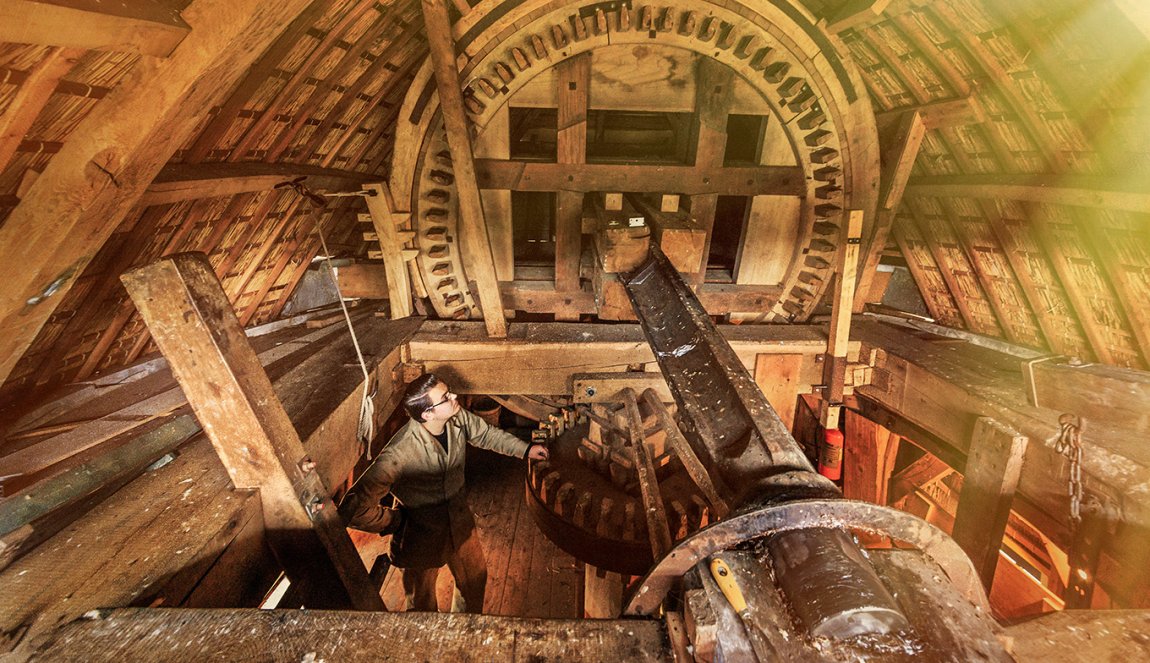 Inside view of a traditional windmill's wooden gear mechanism, with a person examining the structure. Inside view of a traditional windmill's wooden gear mechanism, with a person examining the structure.