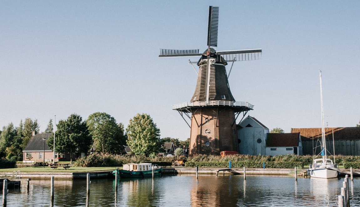 Traditional windmill by the water with boats moored nearby, under a blue sky in a serene setting. Traditional windmill by the water with boats moored nearby, under a blue sky in a serene setting.