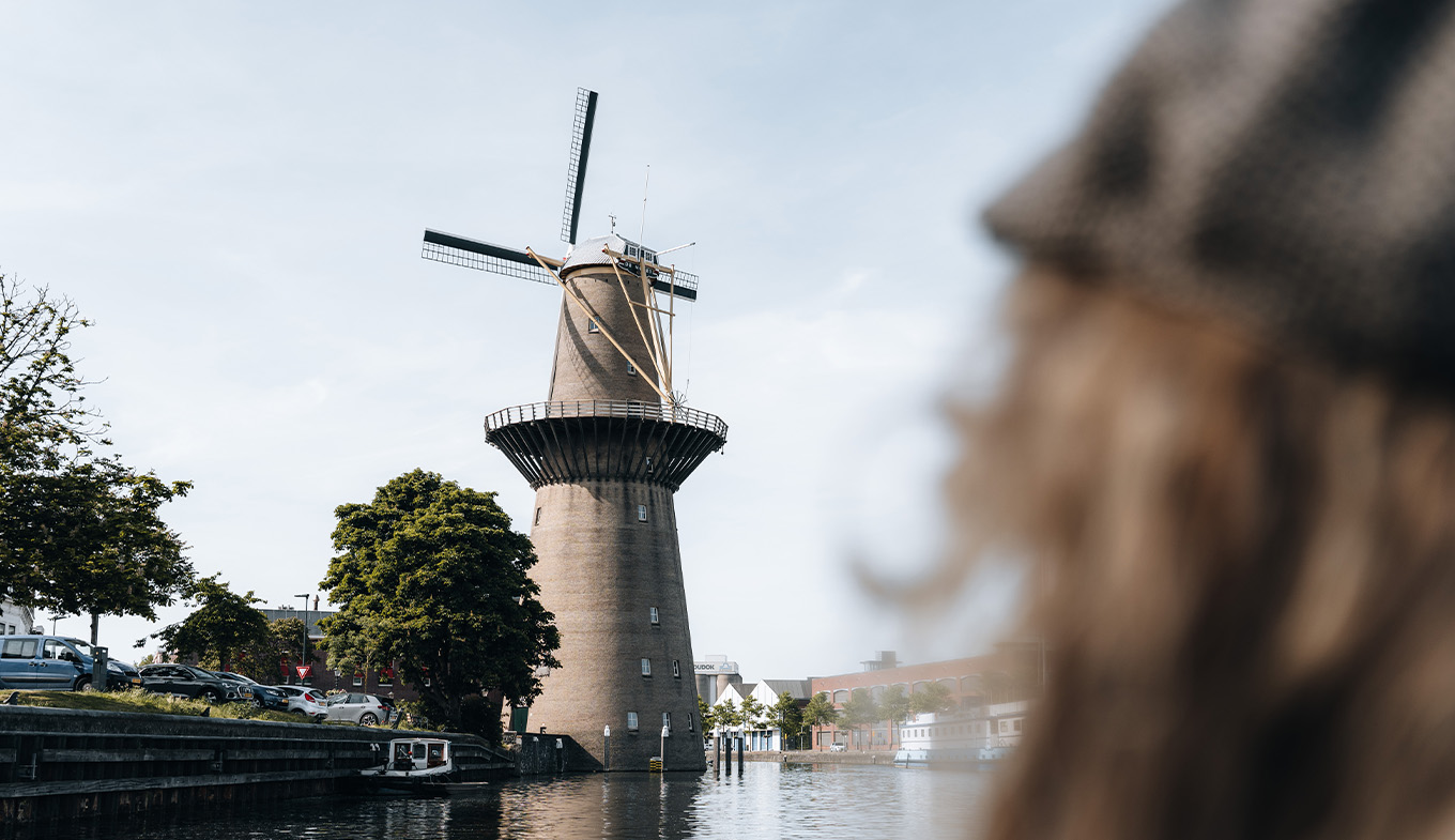 Over-the-shoulder view of a person gazing at 'De Nolet' windmill by a canal Over-the-shoulder view of a person gazing at 'De Nolet' windmill by a canal